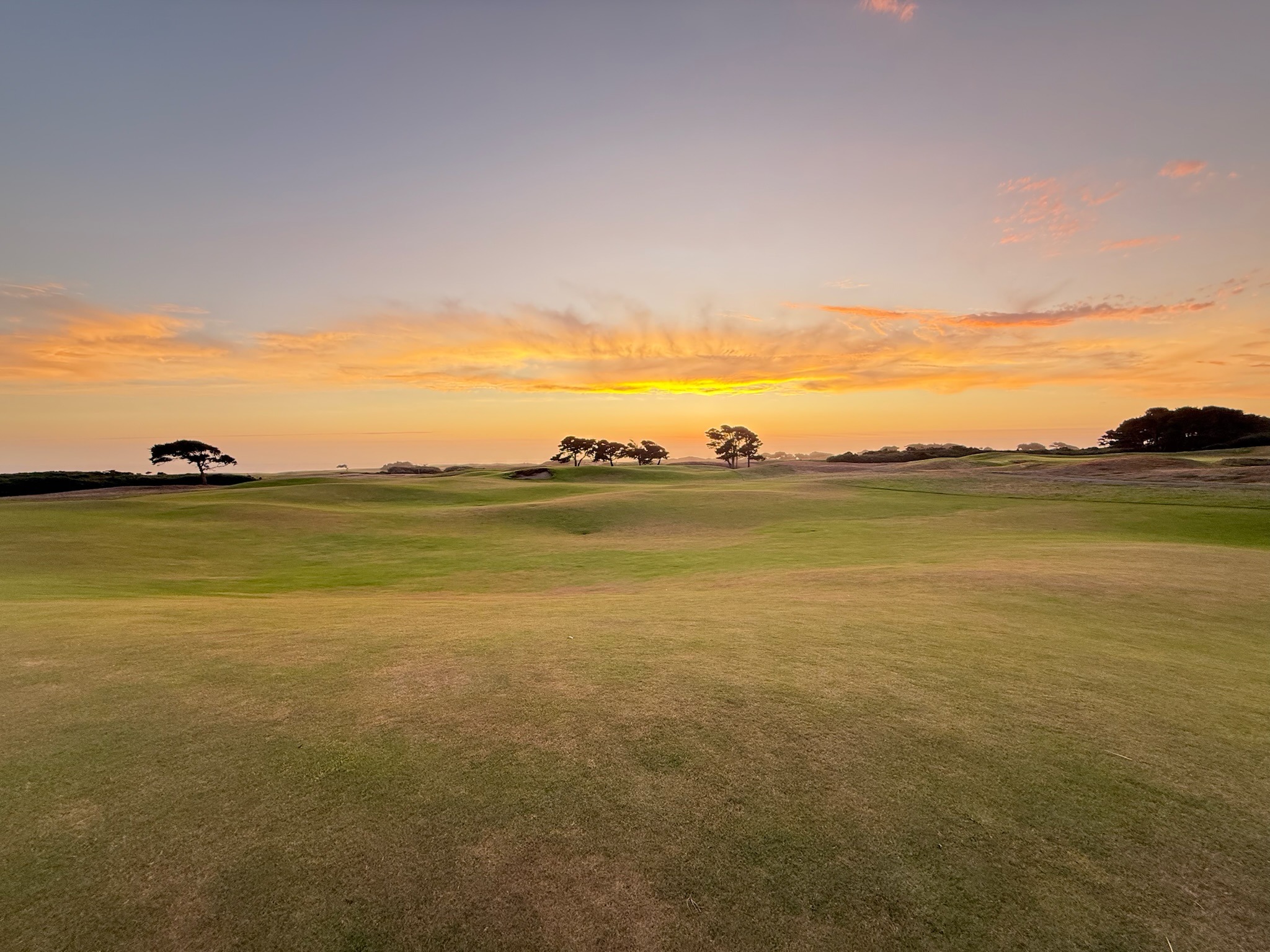 A sweeping Bandon Dunes links vista at golden hour, the sun breaking through cloud over the open course to the ocean